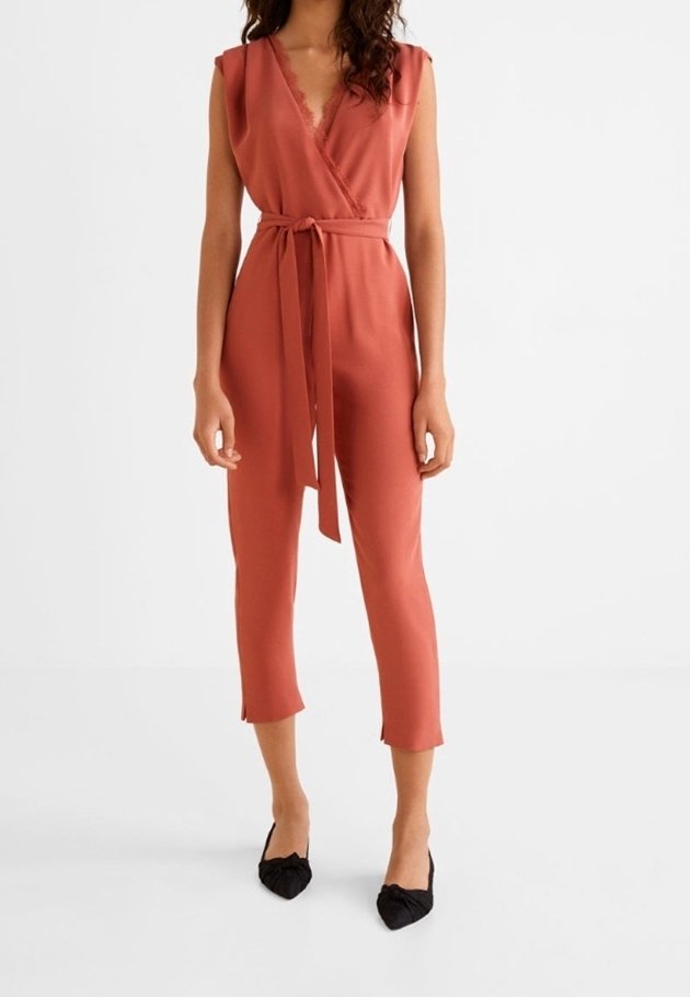 Femme portant une combinaison sans manches couleur rouille avec col en V, ceinture à la taille, jambes raccourcies et ballerines noires pointues.