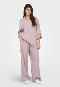 Ensemble deux pièces léger et ample de couleur violet clair, comprenant un haut à col en V avec des manches retroussées et un pantalon à jambes larges, fabriqué dans un tissu texturé.