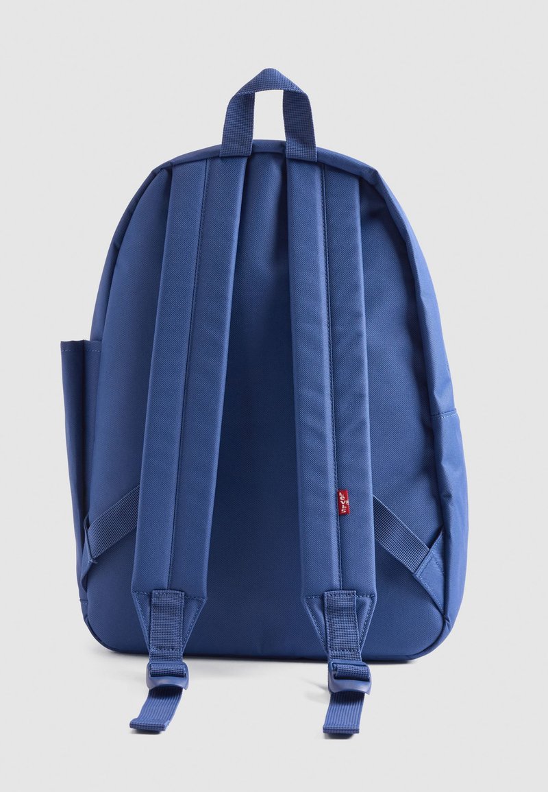 Mochila de tela azul con correas de hombro ajustables y acolchadas y un asa en la parte superior, vista desde atrás sobre un fondo liso.