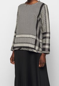 Top a maniche lunghe bianco e nero con motivo geometrico, scollatura rotonda e vestibilità comoda, abbinato a una gonna nera plissettata.