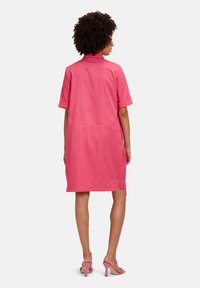 Rosa Hemdkleid mit kurzen Ärmeln und Kragen, aus glattem Stoff gefertigt, mit geradem Schnitt und seitlichen Schlitzen für Bewegungsfreiheit.