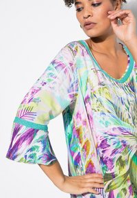 Lätt, flerfärgad kaftan med en luftig passform. Har blommönster i lila, grön och blå, med en turkos detalj vid ärmarna.