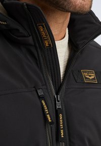 Black jacket made of smooth fabric, featuring dual zippers with PME Legend branding and textured accents on the collar and chest.