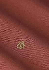 Baumwollstoff in einem tiefen Terrakotta-Ton mit strukturierter Oberfläche, verziert mit goldgesticktem Muschelmuster.