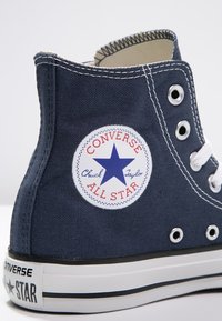 Granatowe, najwyższe trampki Converse All Star z białymi sznurówkami, naszywką z logiem, metalowymi oczkami i białą gumową podeszwą w czarne paski.