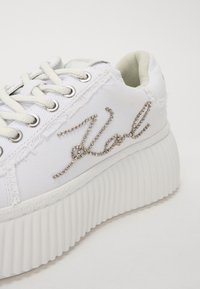 Sneaker bianca in tela con suola bianca a coste, bordi sfrangiati e un scintillante accento "V" argentato. Presenta occhielli e lacci argentati.