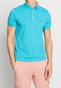 Turkos polo-shirt i mjuk bomull, med en treknappslå, korta ärmar och en liten logotyp på bröstet.