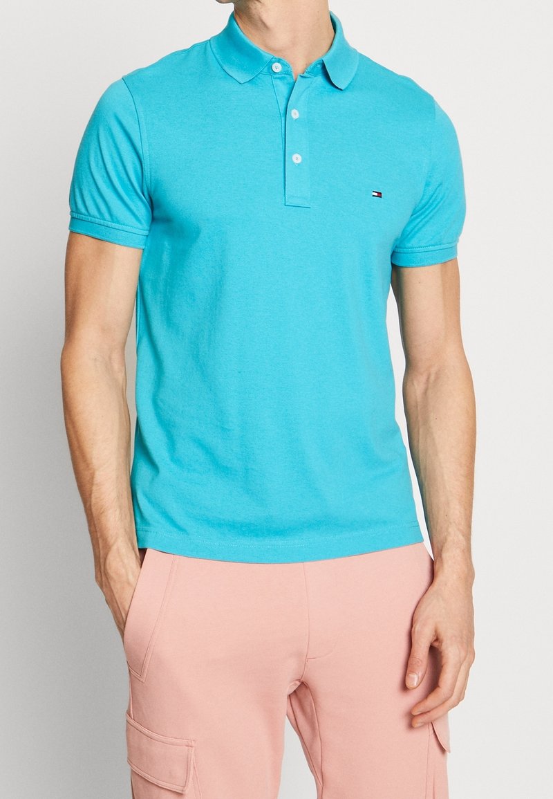 Turkos polo-shirt i mjuk bomull, med en treknappslå, korta ärmar och en liten logotyp på bröstet.