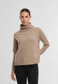 Beige Rollkragenpullover aus weichem Stoff, mit geripptem Saum und gerippten Bündchen. Das Design enthält ein kleines Logodetail an der Seite.