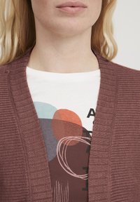 Bordo juostos kardiganas su atviru priekiniu dizainu, užsivilktas ant balto marškinėlio, kuriame vaizduojami abstraktūs raudoni, mėlyni ir rudi apskritimai. Lygi tekstūra.