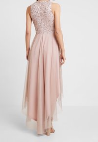 Długa różowa sukienka z wyszywaną górą, przezroczystą nakładką, dopasowanym pasem i zwiewnym dołem, który opada w dłuższy tylny brzeg.