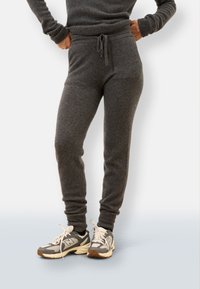 Szare spodnie dresowe wykonane z miękkiego materiału, z regulowanym pasem na sznurki, zwężanymi mankietami, w połączeniu z szaro-kremowymi butami sportowymi.