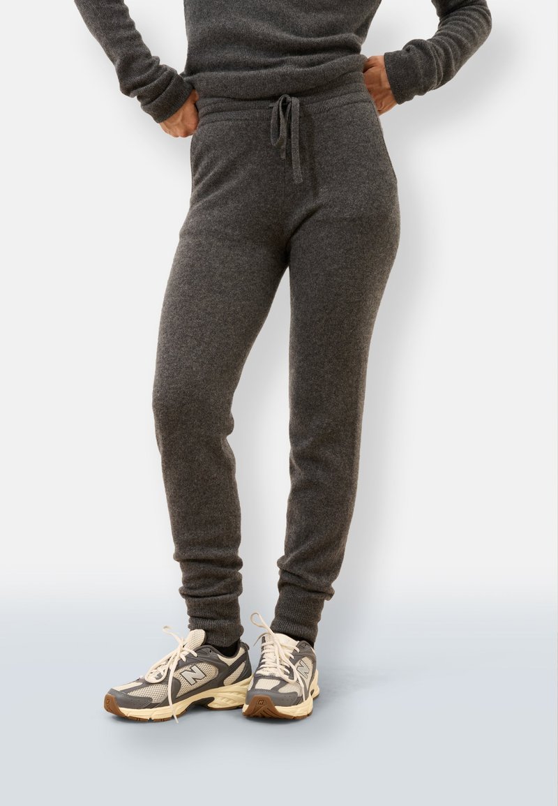 Szare spodnie dresowe wykonane z miękkiego materiału, z regulowanym pasem na sznurki, zwężanymi mankietami, w połączeniu z szaro-kremowymi butami sportowymi.