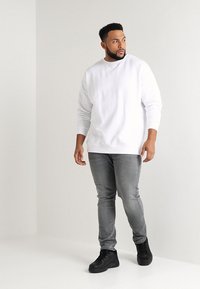 Witte sweatshirt met lange mouwen, grijze slim-fit jeans en zwarte sneakers. Gladde textuur, ontspannen pasvorm en minimalistisch ontwerp.