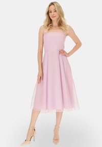 Jasnoróżowa sukienka bez ramiączek z przezroczystego materiału, z dopasowanym gorsetem i zwiewną spódnicą. Połączona z cielistymi szpilkami z ostrym noskiem.