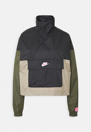 Schwarze, beige und olivgrüne Nike Windjacke mit hohem Kragen, Frontklappentasche und pinkem Logo auf der Brust und am linken Ärmelbündchen.