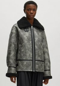 Graue Kunstlederjacke mit schwarzem Fellkragen, Reißverschluss und schwarzen Akzenten. Mit weit geschnittenen Ärmeln und einer strukturierten Oberfläche.