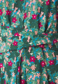 Zielona tkanina z kwiatowym wzorem, zawierająca różowe i czerwone kwiaty, jasnoróżowe pąki oraz zielone liście na niebieskim tle; detal z plisowanym wzorem.