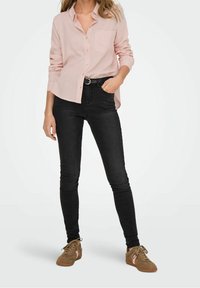Camisa de botón de manga larga color rosa claro con un bolsillo en el pecho, combinada con jeans ajustados negros y zapatillas marrones con toques rosas.