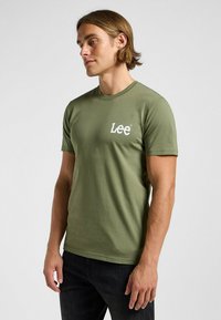 Oliwkowa bawełniana koszulka z krótkim rękawem, okrągłym dekoltem i białym logo "Lee" na lewej piersi. Gładka tekstura materiału.