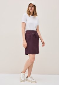 Gonna viola al ginocchio con cintura elastica e cordino, abbinata a una maglietta bianca a maniche corte e sneaker bianchi.