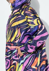 Veste imperméable colorée avec un motif tourbillon en violet, jaune et rose sur fond marine. Comprend des poches et une capuche.