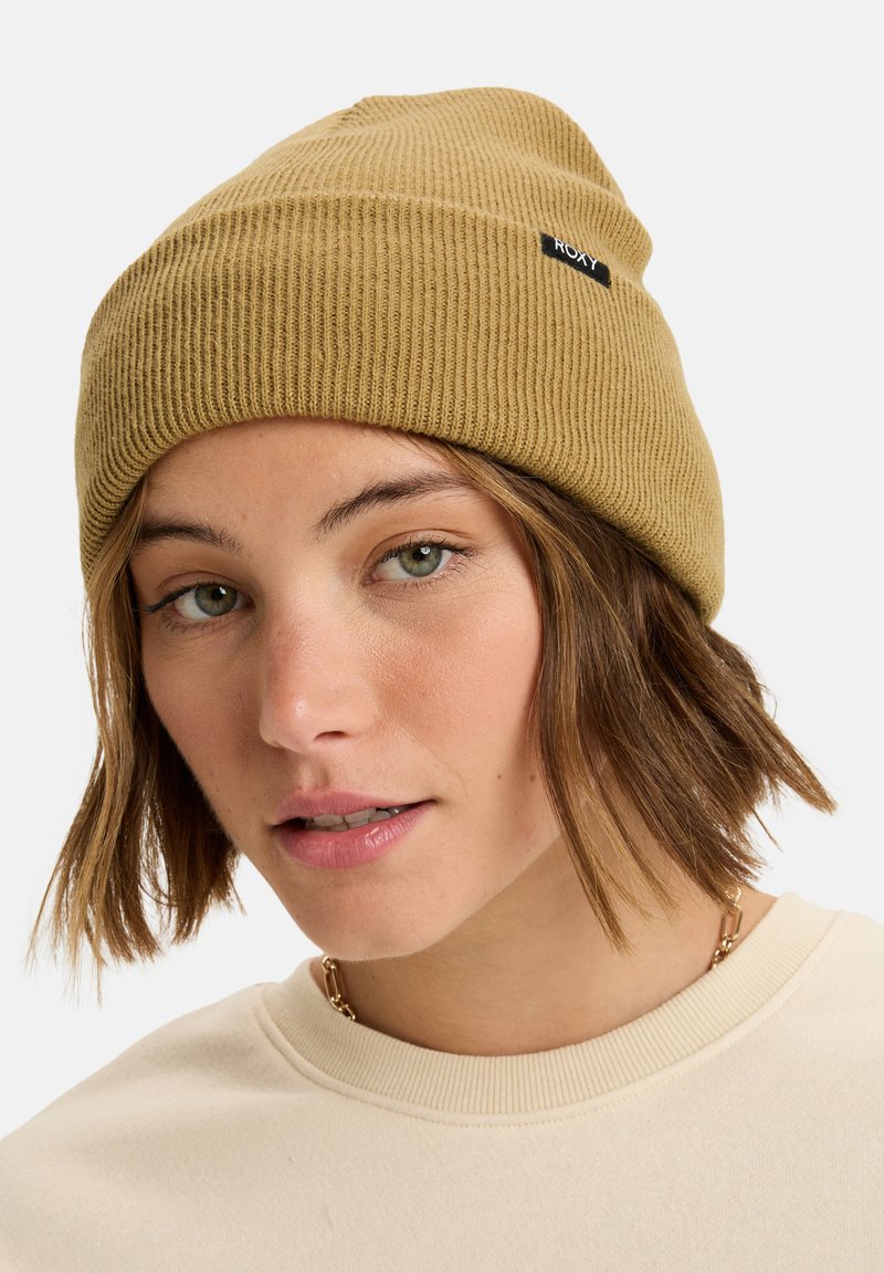 Beige ribbed beanie hat featuring a small black Roxy logo. The material appears textured and stretchy, fitting snugly on the head.