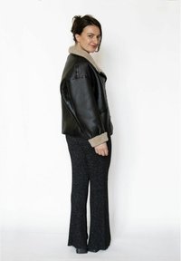 Sort læderjakke med beige kunstpels-krave og manchetter, kombineret med sorte udsvingede bukser. Glat tekstur, afslappet pasform og dristigt design.