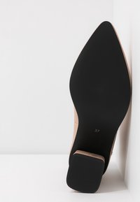 Semelle d'une chaussure beige à bout pointu avec semelle noire et talon bloc, taille 37, reposant contre une surface blanche.