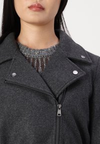 Grå uldblandingsjakke med en klippette krave, sølvhardware detaljer og lynlåsforlukning, lagd over en tekstureret grå striktrøje.