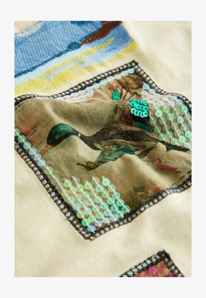 Bēša audums ar teksturētu dizainu, kurā zaļās fliteru pērlītes ir sakārtotas rakstā ap iespiestu pīles attēlu uz nomierinātas krāsas fona.