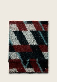 Couverture en laine avec un motif géométrique comportant des couleurs rouge, vert foncé et gris, texture douce, et une étiquette noire dans le coin.