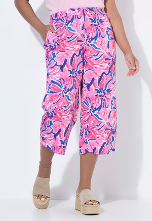 Kvinde iført pink, lilla og blå blomstrede vidde ben cropped bukser med beige platform sandaler og gul tå-neglelak.