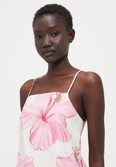 Vestido floral con grandes patrones de hibisco rosa sobre un fondo blanco, con finas tiras de espagueti y una textura de tela suave.