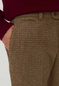 Brown checkered trousers made of textured fabric, featuring a straight cut, side pockets, and a sleek waistband with a button detail.