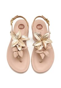 Sandalias beige con acentos florales, con pétalos de tela y metal dorado. Correa ajustable con herrajes dorados, suela plana.