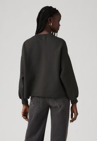 Dark sweater made of soft fabric, featuring a relaxed fit, long puff sleeves, and a crew neckline, paired with gray denim pants.