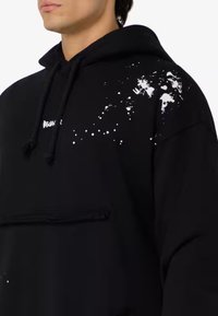Felpa nera in misto cotone, caratterizzata da un motivo testurizzato a macchie di vernice bianca su una spalla. Include una tasca frontale e cappuccio con cordino.
