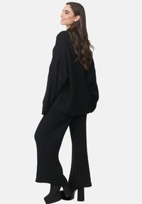 Zwarte ribgebreide trui met oversized mouwen, gecombineerd met bijpassende ribgebreide broek. Model draagt chunky zwarte platformhakken.