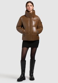 Jachetă pufosă maro, lucioasă, cu guler �înalt, având panouri cusute și două buzunare frontale. Purtați-o peste o fustă neagră cu dungi și cizme negre.