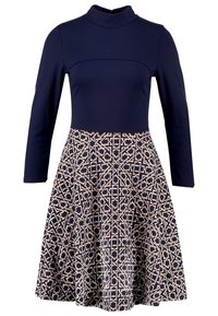 Robe bleu marine à manches longues avec un col montant et une jupe évasée présentant un motif géométrique beige et bleu marine.