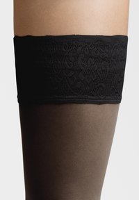 Sort spids gambestøj med et glat, mørkebrunt, gennemsigtigt benafsnit. Tekstureret blomsterdesign på den blonde strop.