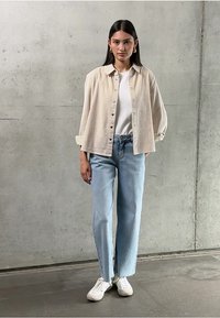 Crème-kleurige button-up shirt, witte t-shirt, lichtblauwe straight-leg jeans en witte sneakers. Zachte textuur, casual stijl.