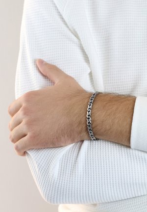 Silver chain bracelet with alternating dark and light links on a wrist, paired with a textured white long-sleeve shirt.
