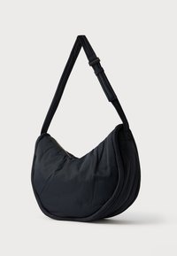 Musta, pehmeä kangasolkainen laukku, jossa kaareva muotoilu. Varustettu leveällä hihnalla ja vetoketjulla, korostaen sileää rakennetta.