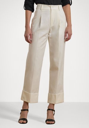 Bequeme Hose aus cremefarbenem Stoff mit Falten, hoher Taille und umgeschlagenen Säumen. Kombiniert mit schwarzen Sandalen mit Riemchen.