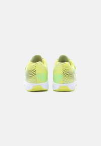 Ζευγάρι αθλητικά παπούτσια κίτρινο-πράσινου χρώματος με λευκές σόλες, εμφανιζόμενα από πίσω σε ανοιχτό γκρίζο φόντο.