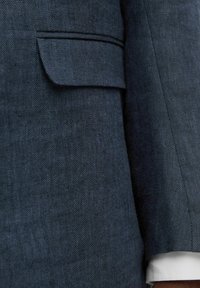 Blazer in lino blu con una finitura texturizzata, dotato di tasca a filetto e di un polsino bianco a contrasto che spunta dalla manica.