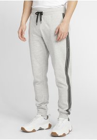 Grå träningsoverallsbyxor med svarta sidosträck, elastisk midja med dragsko, smal passform. Matchad med vita sneakers med brunt sula.