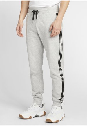 Grå joggebukser med svarte side-streker, elastisk midje med snor, tapered fit. Sammen med hvite joggesko med brun såle.